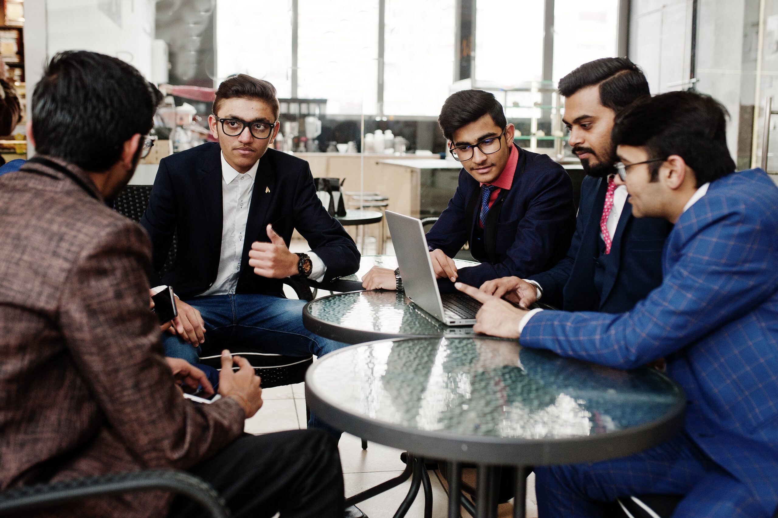 Group of five indian business man in suits sitting at office on cafe and looking at laptop.